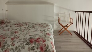 Quarto com colcha florida, vigas de madeira, luminária de chão e cadeira de madeira.