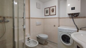 Uma casa de banho compacta com chuveiro, sanita, bidé e máquina de lavar roupa.