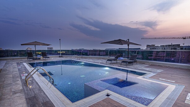 A rooftop pool with a clear view of the city skyline, surrounded by lounge chairs and umbrellas. - Green Park Hotel (Doha)