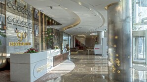 A modern hotel lobby with a reception desk, a large column with star decorations, and a glass elevator. - Green Park Hotel (Doha)