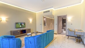 A modern living room with a sofa set, a TV, and a dining area with a table and chairs. - Green Park Hotel (Doha)