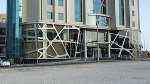 A modern hotel with a curved facade, large windows, and a prominent entrance with a glass canopy. - Green Park Hotel (Doha)