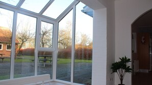Ein Zimmer mit großen Fenstern, einer Bank davor und einer Zimmerpflanze darin.