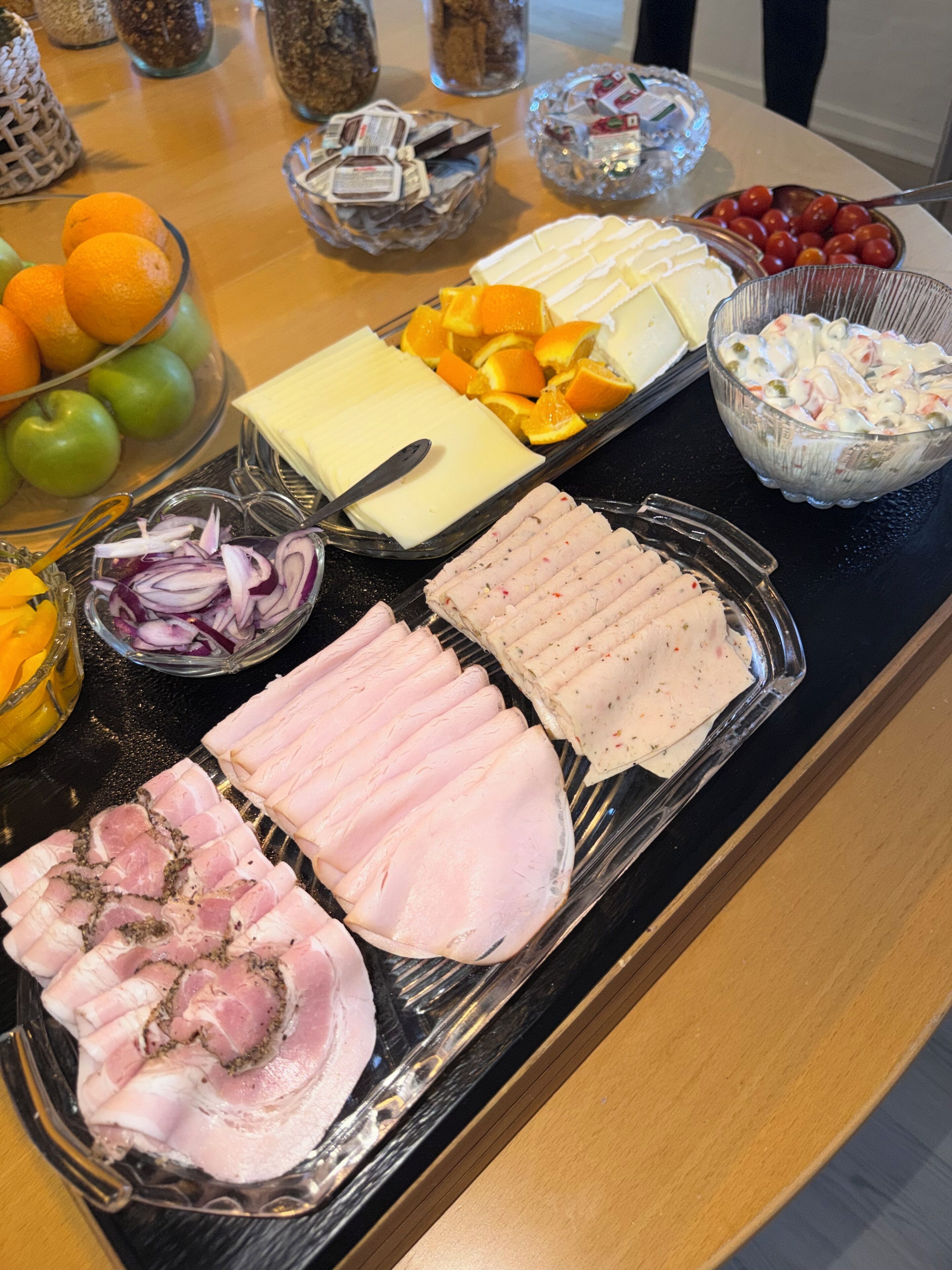 Una mesa de buffet con diversos alimentos, incluyendo carnes frías, quesos, frutas y una ensalada.