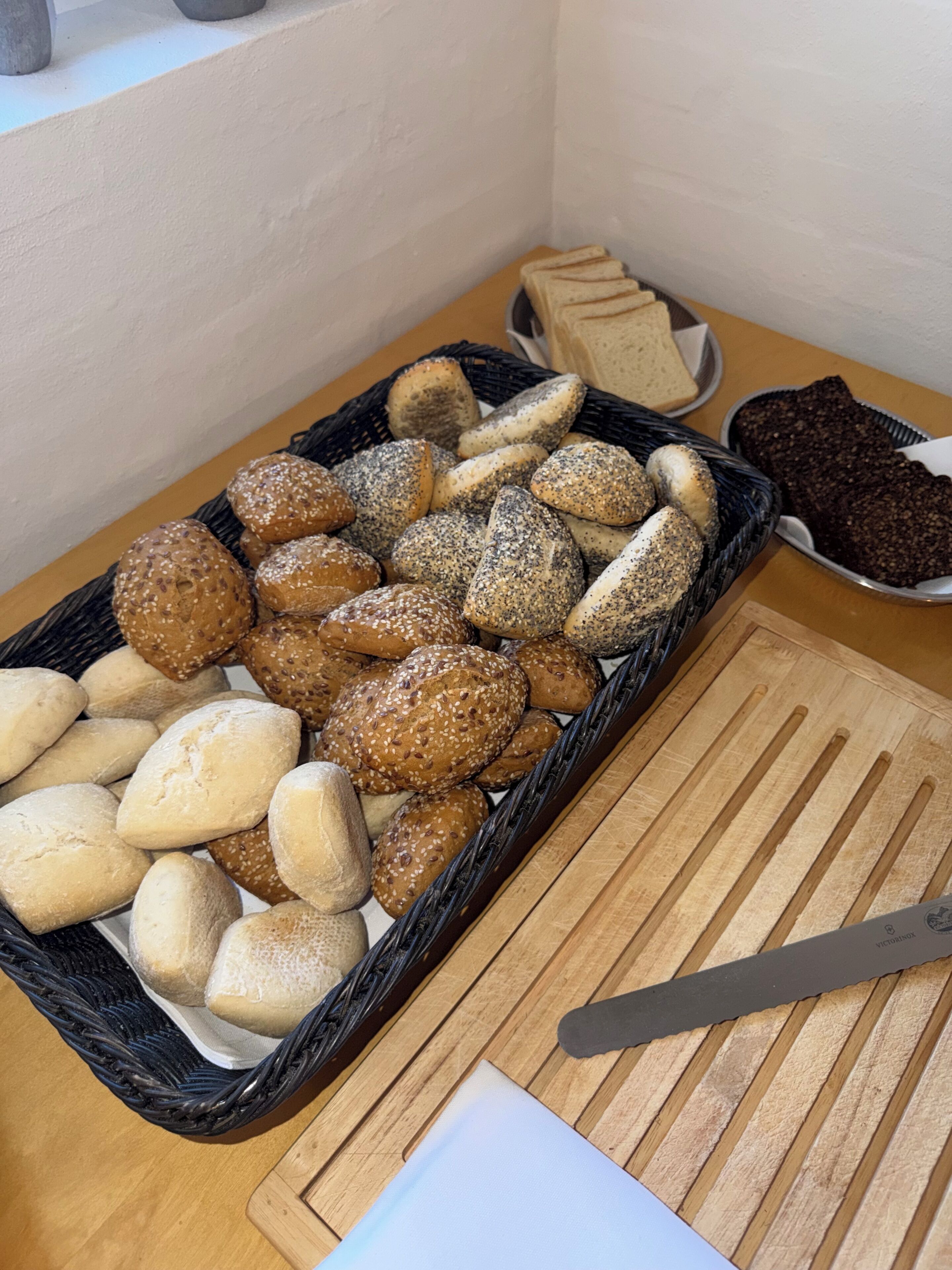 Verschiedene Brotsorten und Gebäck auf einer Tischplatte, darunter ein Korb mit Brötchen und eine Schale mit dunklem Brot.