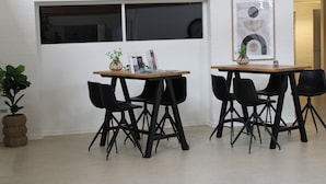 Ein modernes Zimmer mit zwei Tischen und vier schwarzen Stühlen, einer Topfpflanze und einem gerahmten abstrakten Kunstwerk an der Wand.