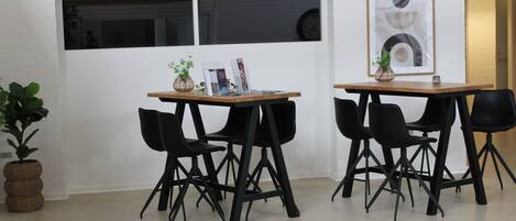 A modern room with two tables and four black chairs, a potted plant, and a framed abstract artwork on the wall.