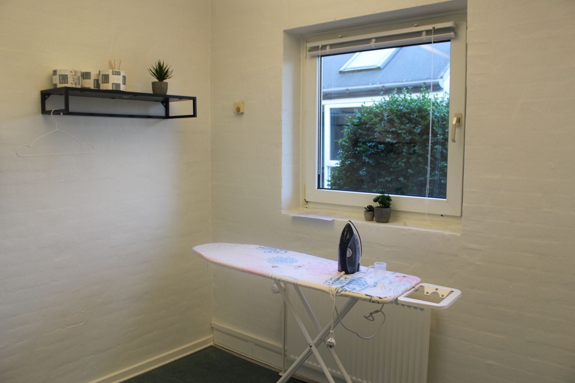 A small room with a window, an ironing board, and a radiator.
