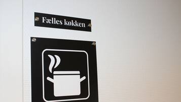 A sign with a coffee pot symbol and the text 'Faelles kökken' indicating a coffee area.