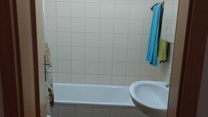 Une petite salle de bain avec une baignoire, un lavabo et des toilettes. Un tapis à rayures recouvre le sol.