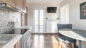 Een moderne keuken met een inbouwoven, een eethoek met een grijze tafel en stoelen, en een televisie die aan de muur is bevestigd.