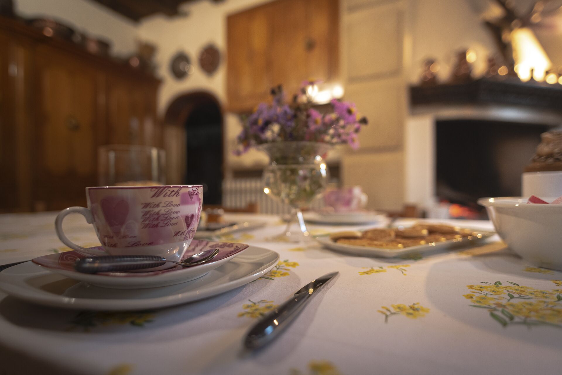 A table set with a teacup, saucer, spoon, and a floral tablecloth.