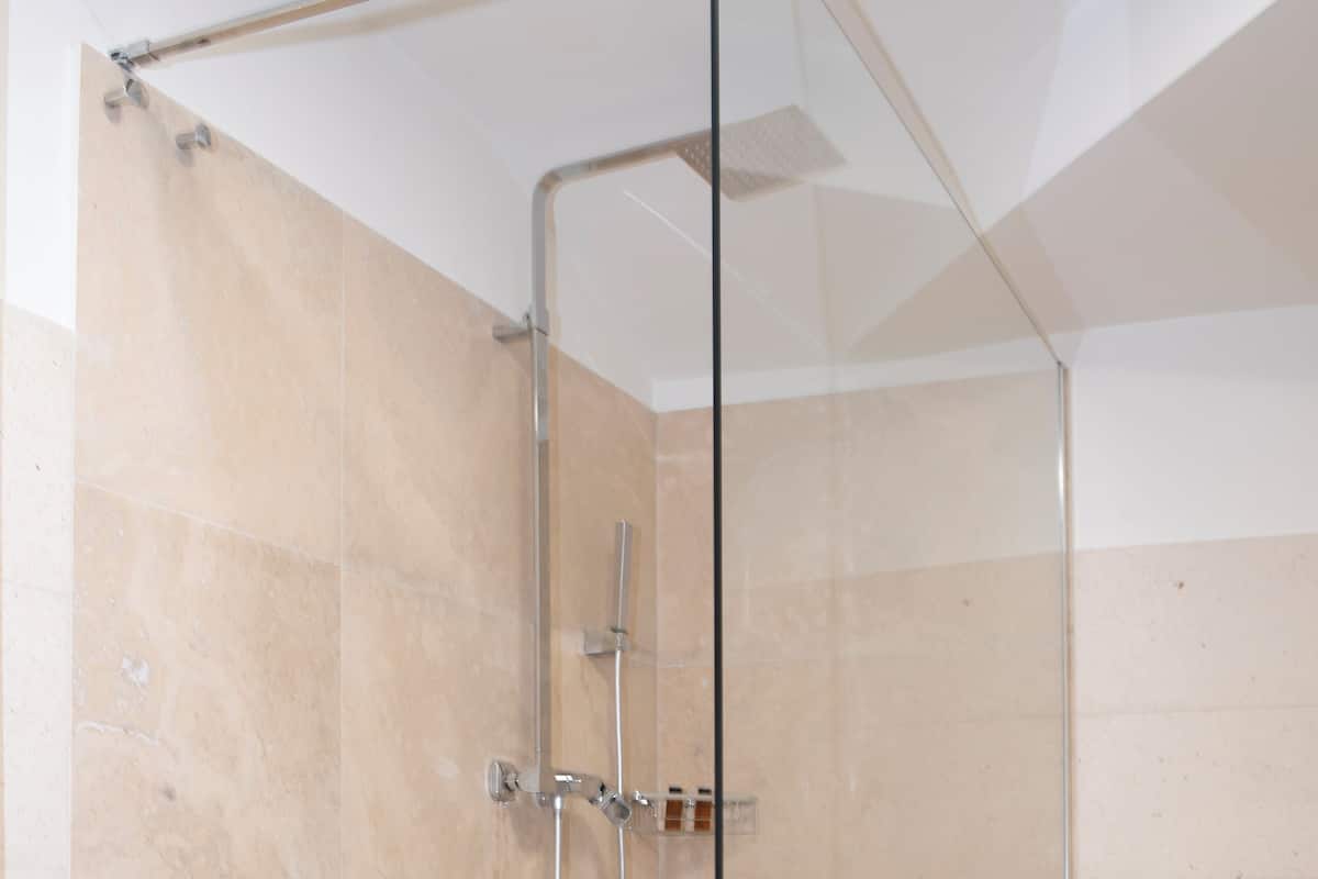 A glass-enclosed shower with a white floor and beige tiles.