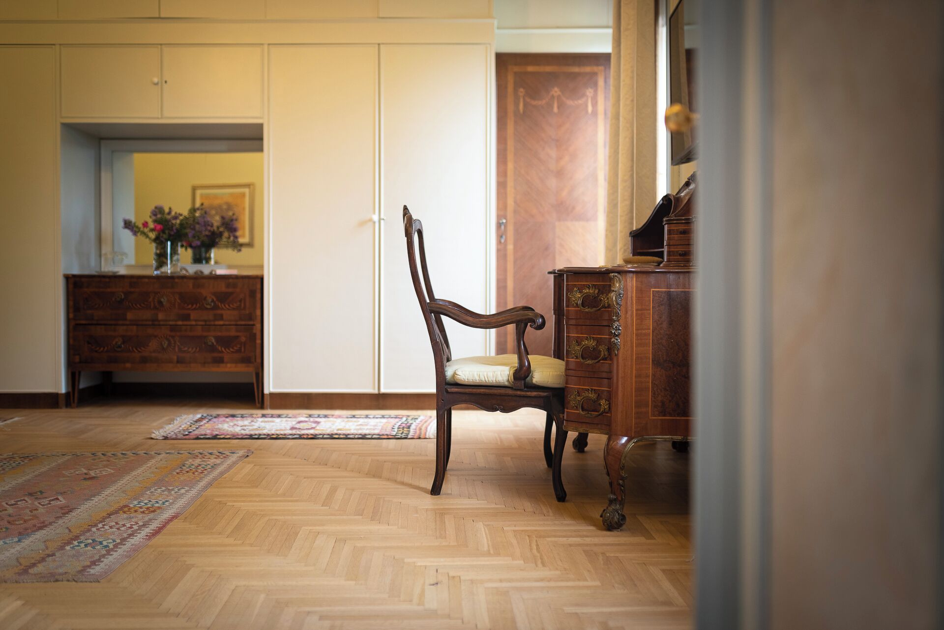 Una stanza con pavimento, sedia e cassettiera in legno, e una porta.