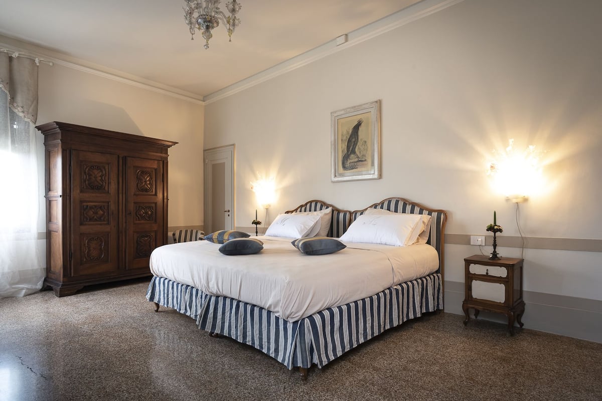 A bedroom with a large bed, two bedside tables, a wooden wardrobe, and a chandelier.