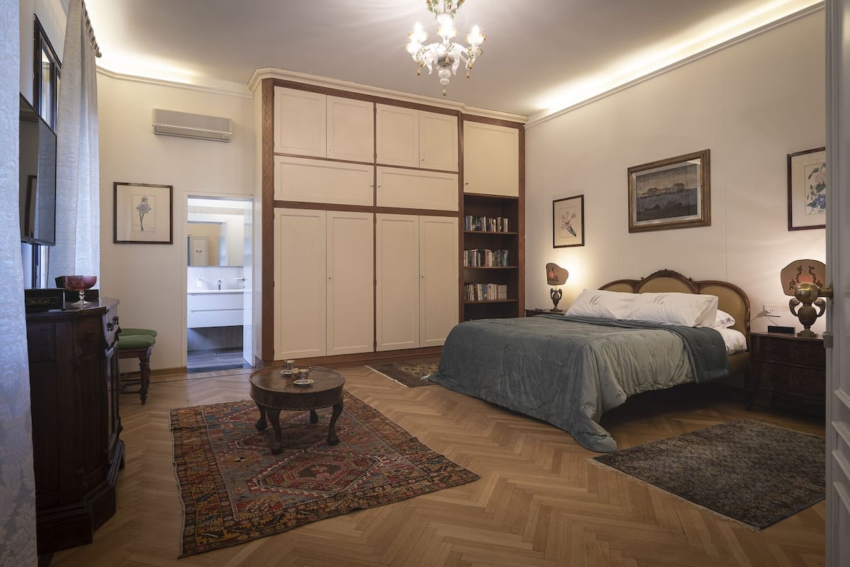 A bedroom with a bed, a nightstand, a bookshelf, a dresser, a mirror, and a chandelier.