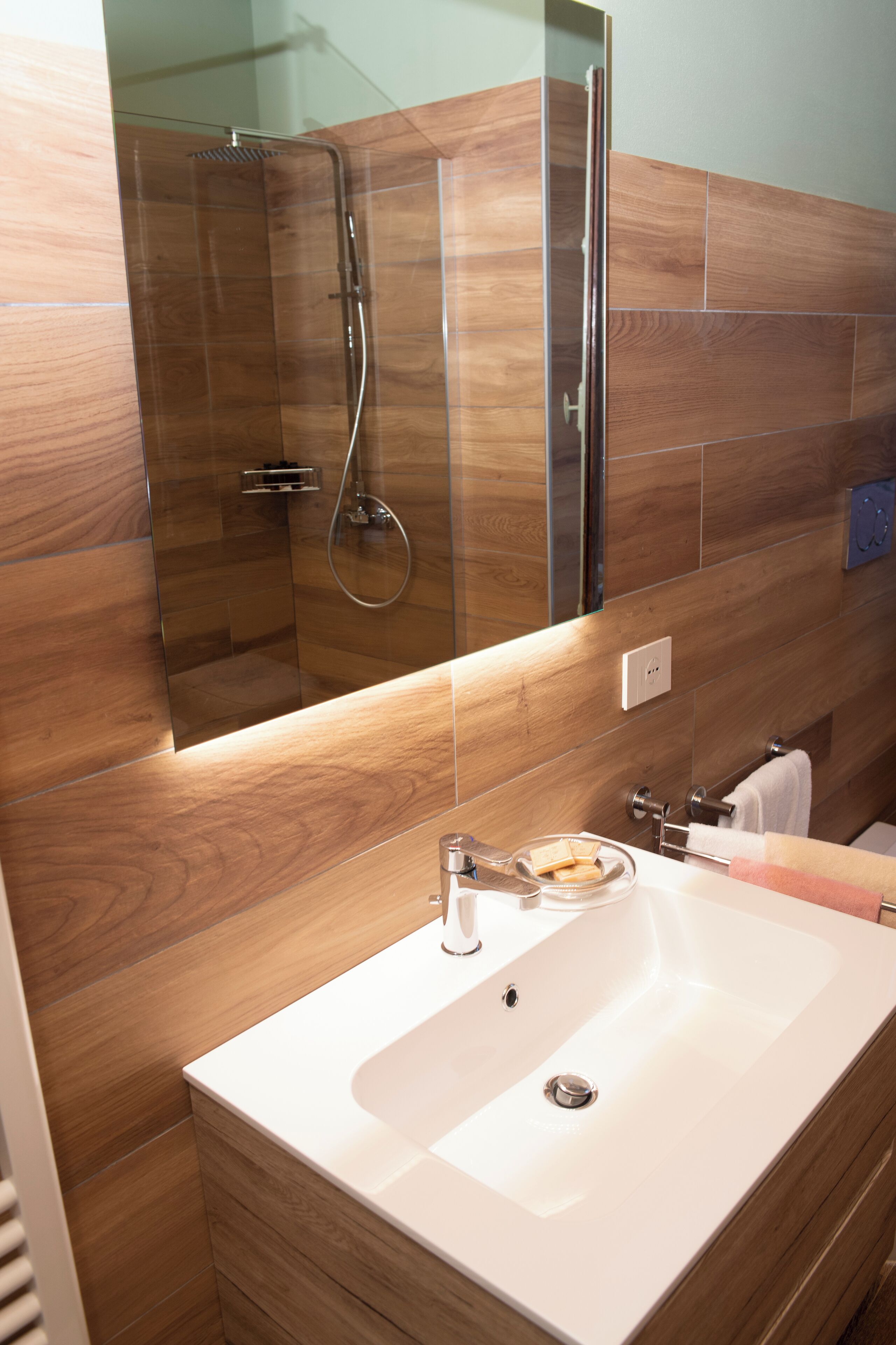 A modern bathroom with a glass-enclosed shower, a white sink, and wooden wall tiles.