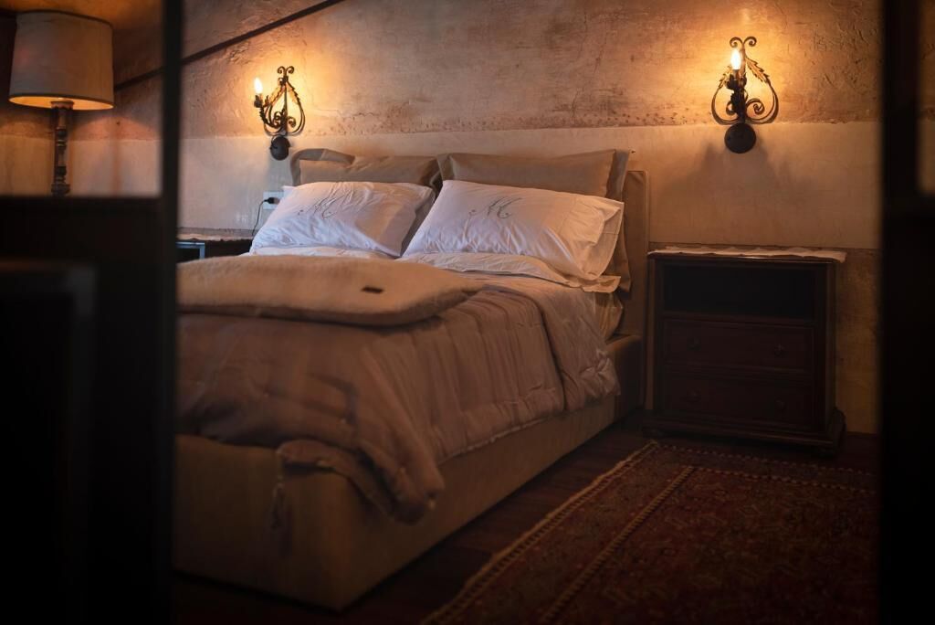 A bedroom with a large bed, two wall-mounted lamps, a nightstand, and a rug.