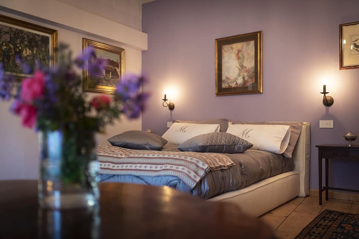 A bedroom with a bed, bedside tables, wall-mounted lamps, and framed artwork.