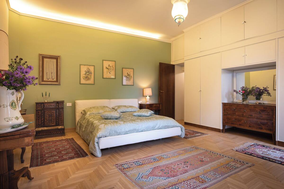 A bedroom with a bed, wooden dresser, and a large mirror.