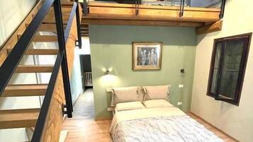 A bedroom with a bed, a nightstand, a lamp, a framed picture on the wall, and a staircase.