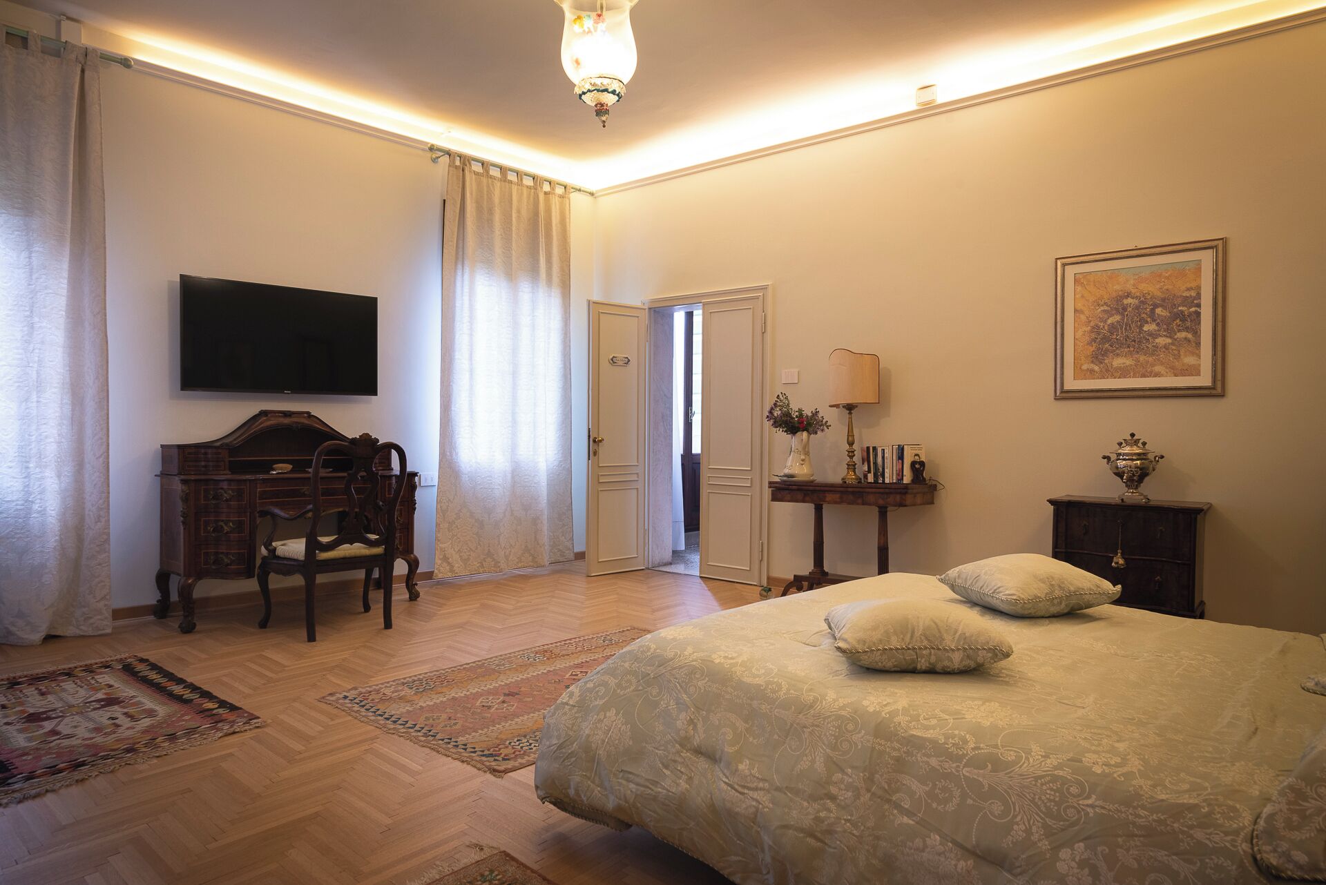 A bedroom with a bed, a desk, a chair, a television, and a door leading to another room.
