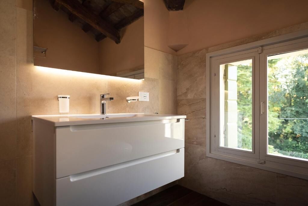 A bathroom with a white vanity, a mirror, and a window with a view of greenery.