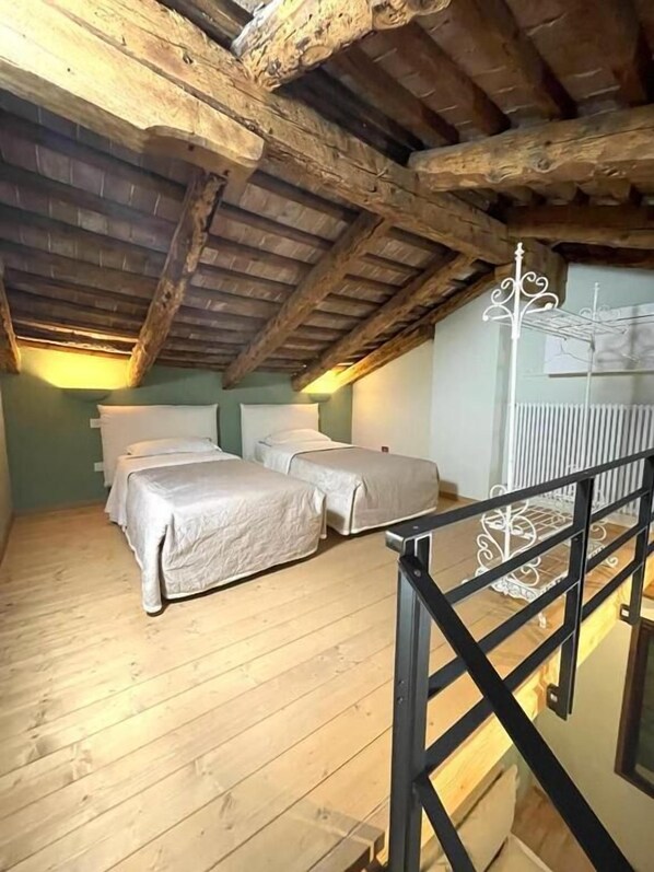 Ein Schlafzimmer mit zwei Betten, Holzbalken an der Decke und einem weißen Metallgeländer.