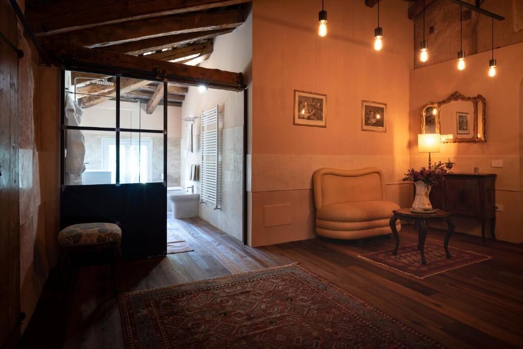 Ein gemütliches Zimmer mit Holzboden, einem gepolsterten Sessel, einem kleinen Tisch mit einer Vase und einem Spiegel an der Wand.