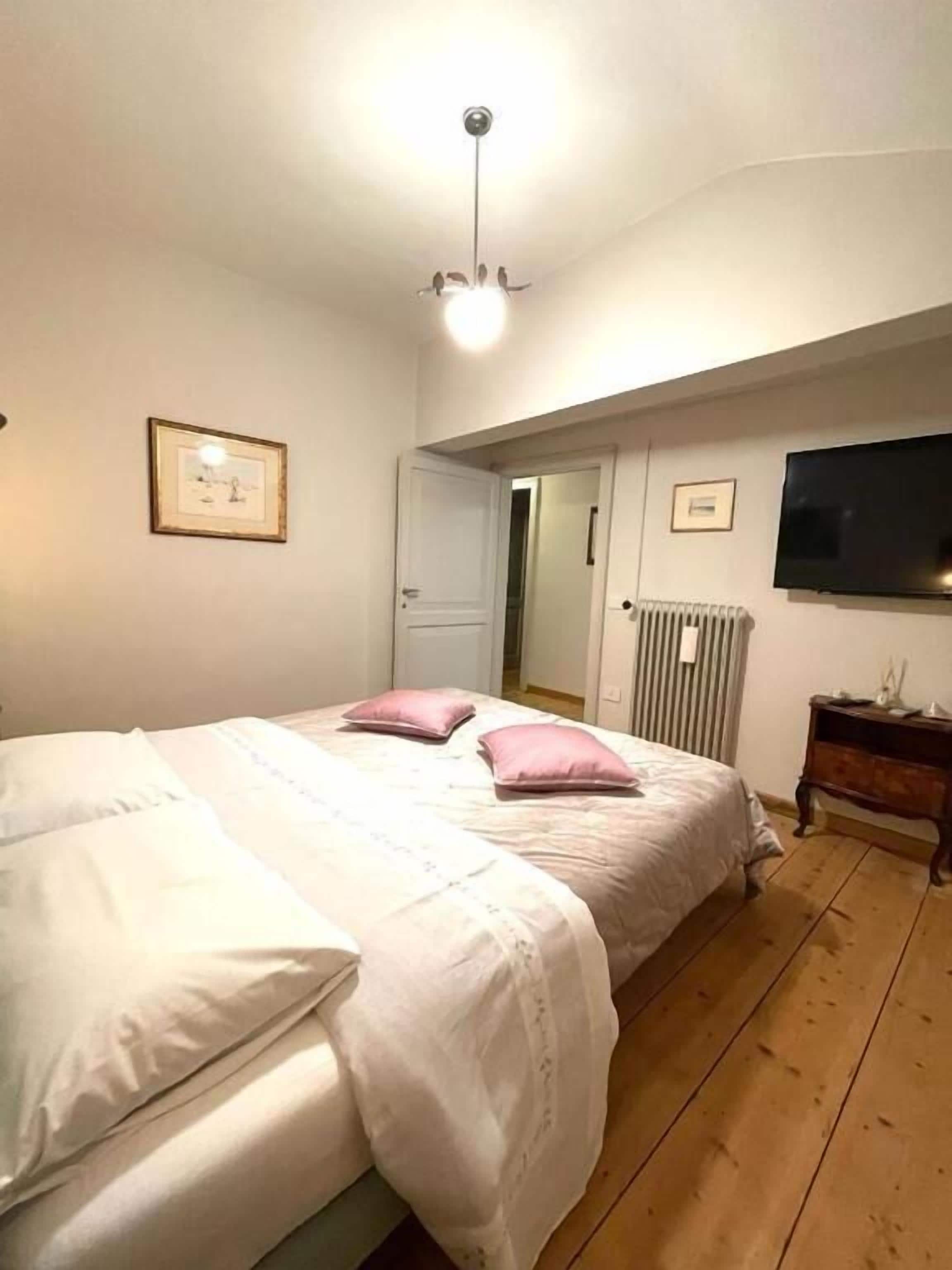 A bedroom with a bed, a radiator, a television, and a door leading to another room.