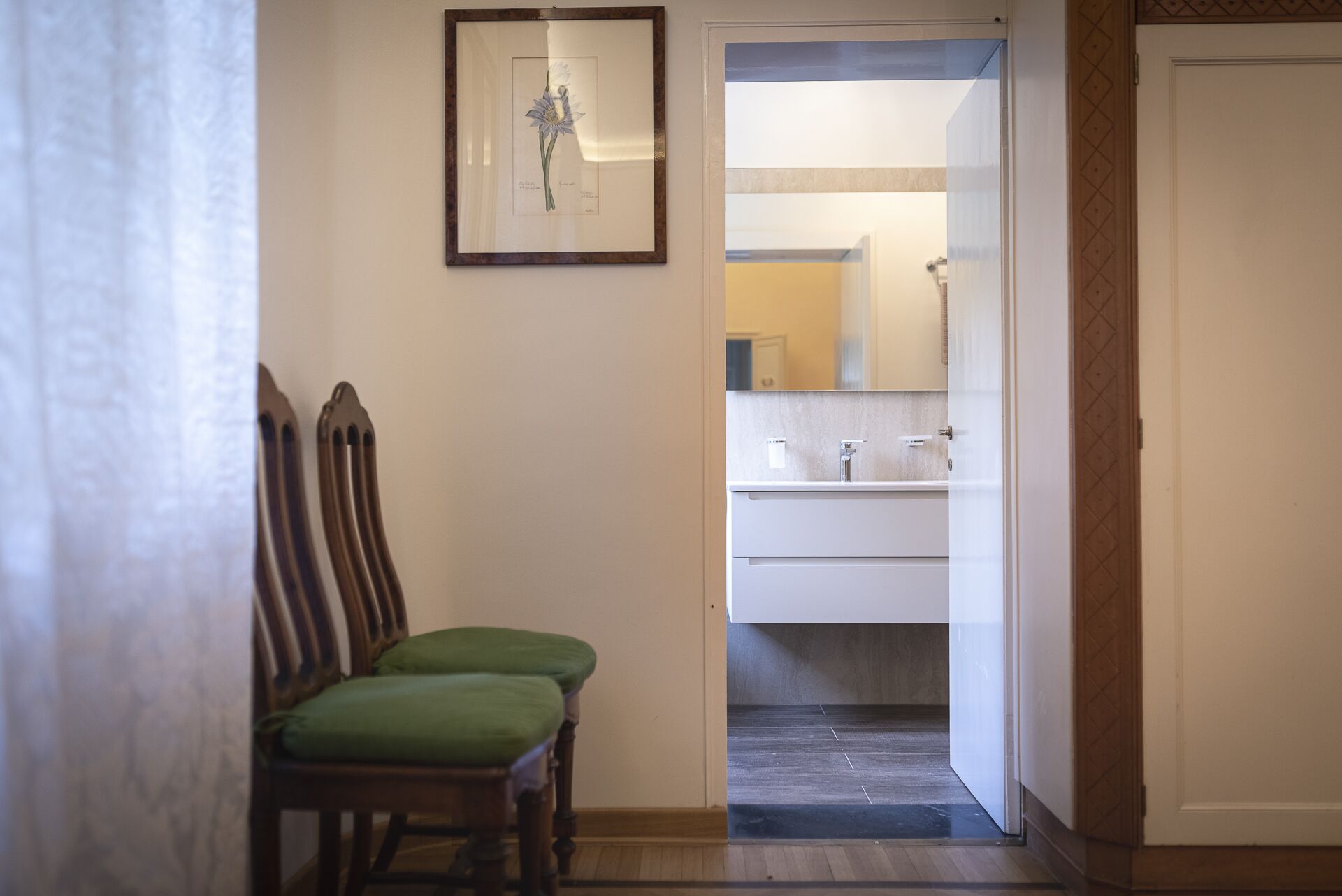 A hallway leading to a bathroom with a sink and mirror. There are two chairs with green cushions.