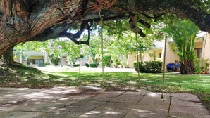 Un espacio al aire libre techado con un columpio, rodeado de follaje y edificios.