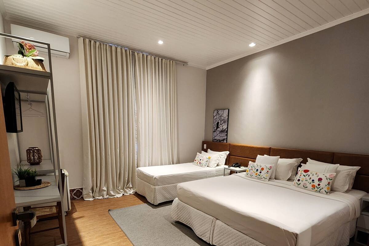 Une chambre d’hôtel moderne avec deux lits, un plancher en bois, une grande fenêtre avec des rideaux, une table de chevet et un téléviseur fixé au mur.