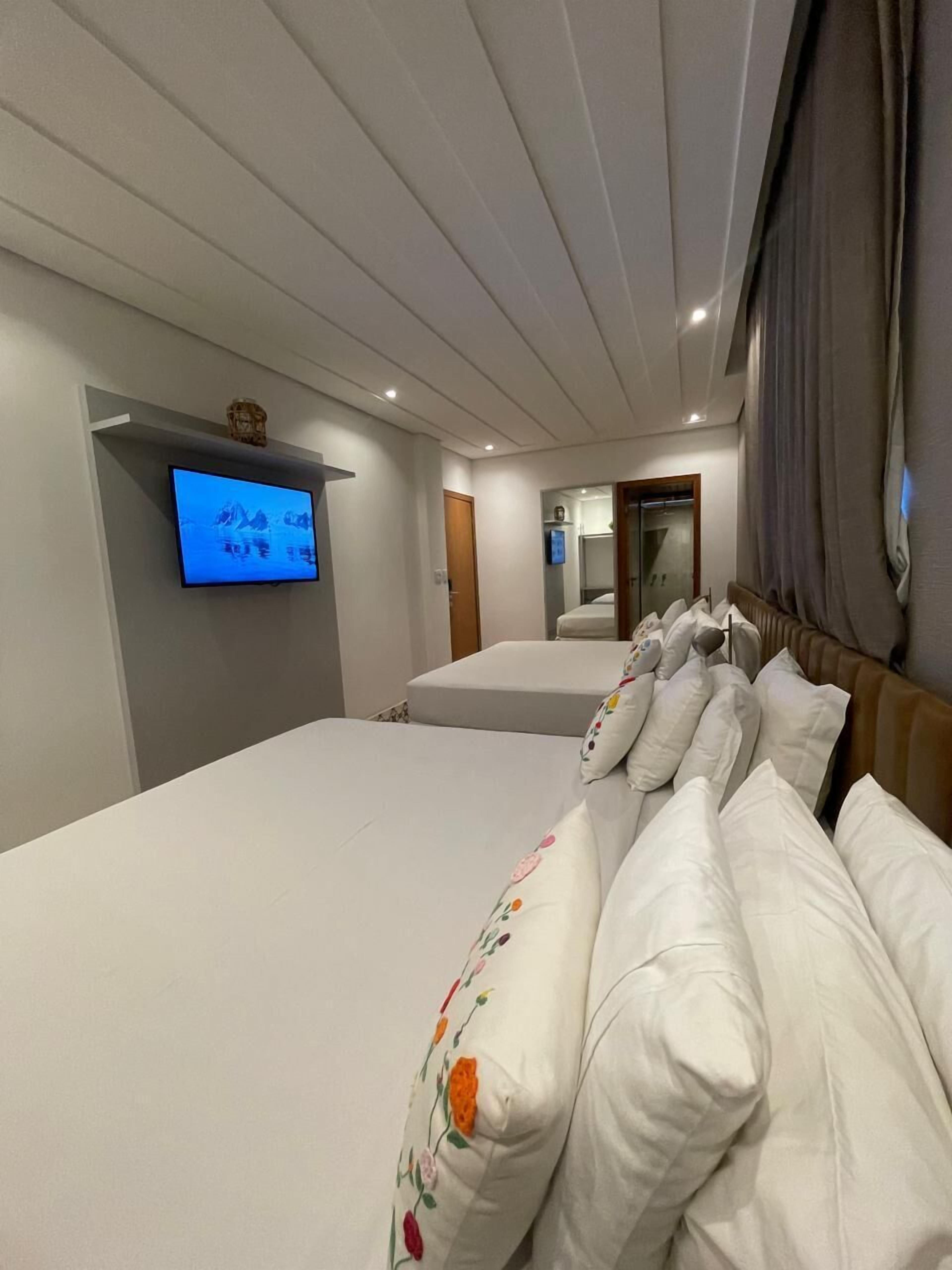 A hotel room with two beds, a television mounted on the wall, and a mirror reflecting the room.