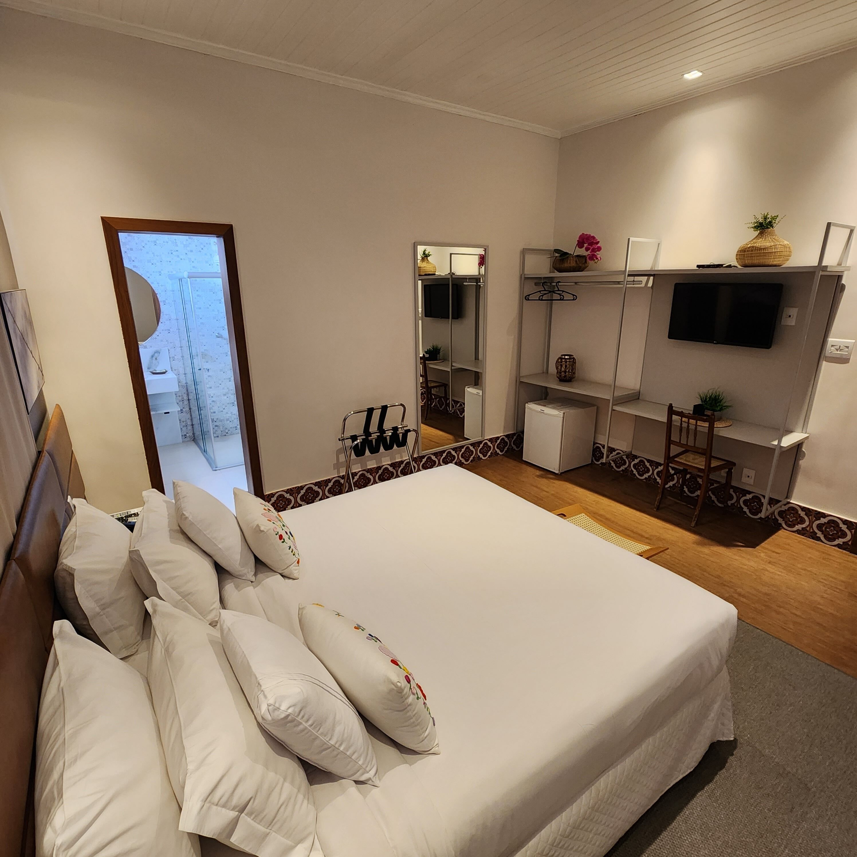 A bedroom with a large bed, a TV mounted on the wall, and a small desk with a chair.