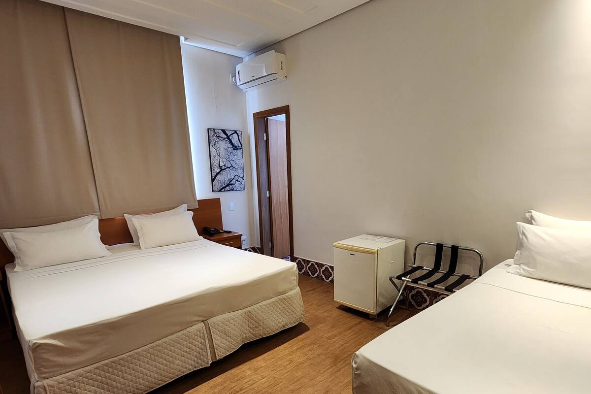 Une chambre d’hôtel avec deux lits, un petit bureau, une chaise, un appareil de climatisation et une porte.