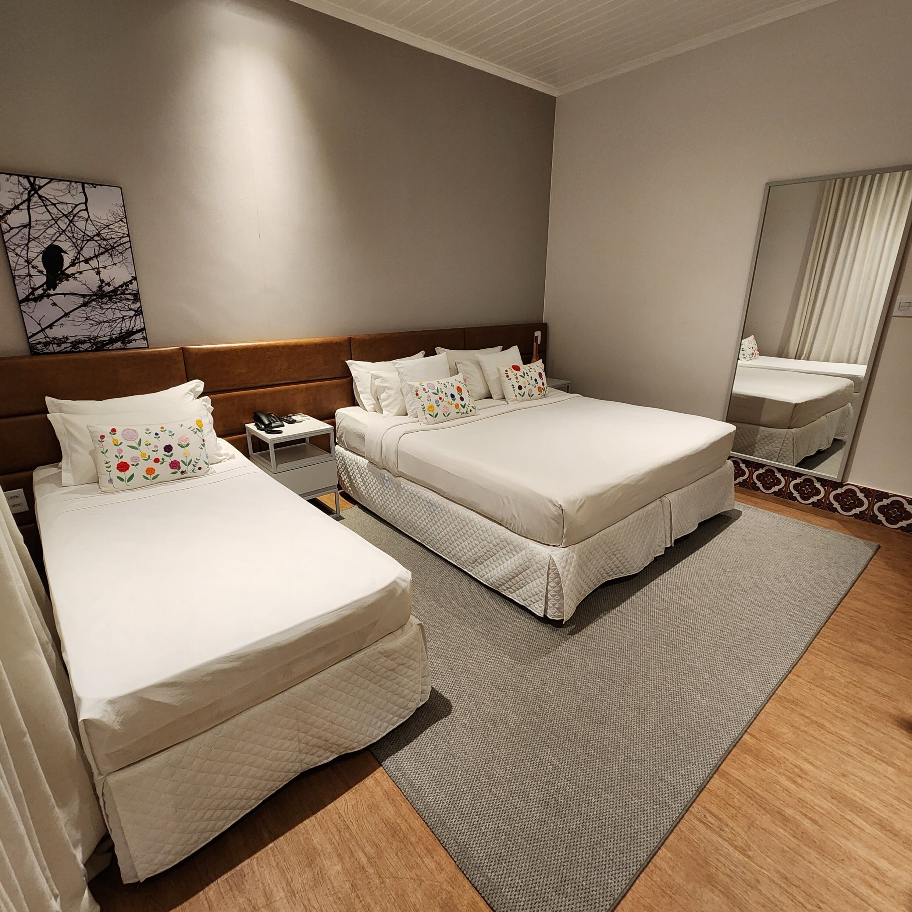 Habitación de hotel con dos camas, una mesita de noche con un teléfono, un espejo y una obra de arte en la pared.