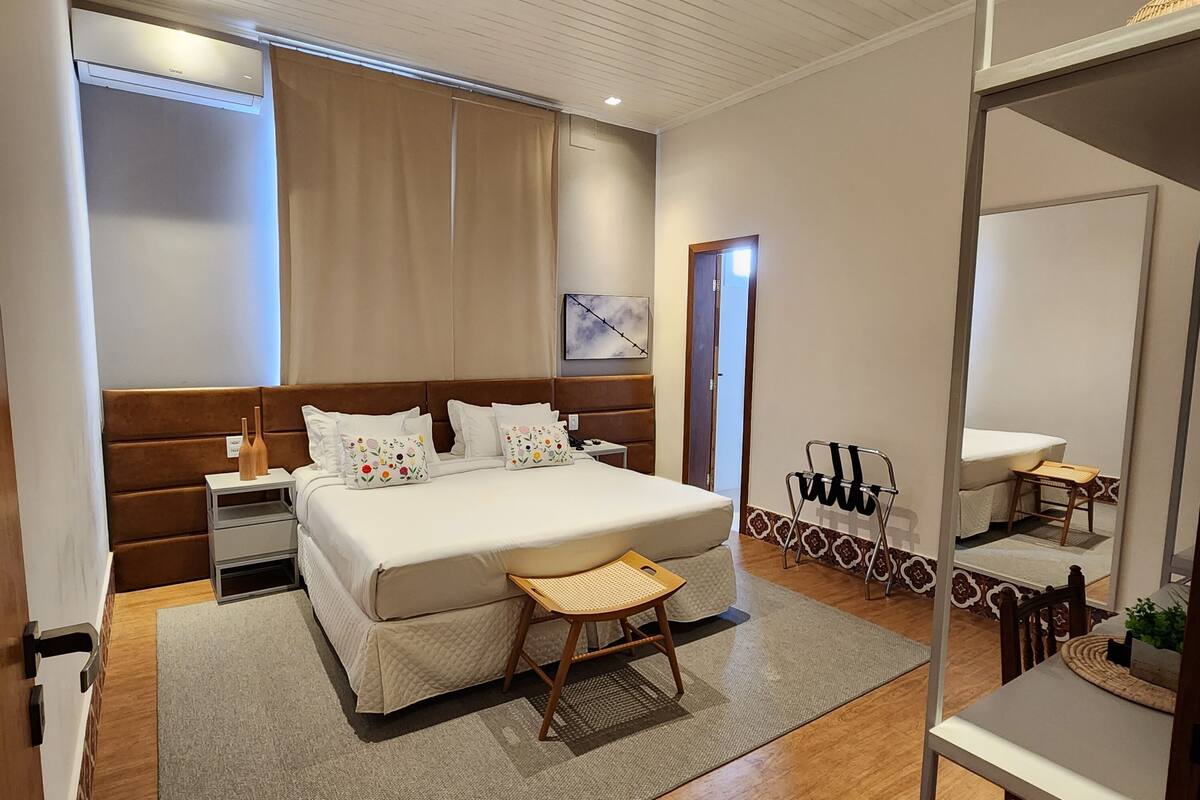 Une chambre moderne avec un grand lit, des tables de chevet, un miroir et un petit coin salon.