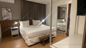 Een moderne slaapkamer met een groot bed, nachtkastjes, een bankje en een spiegel.