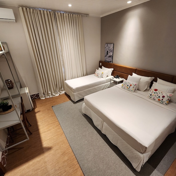 A hotel room with two beds, a small table, a chair, a shelf with decorative items, and a window with curtains. - Hotel Estilo de Minas (Diamantina)