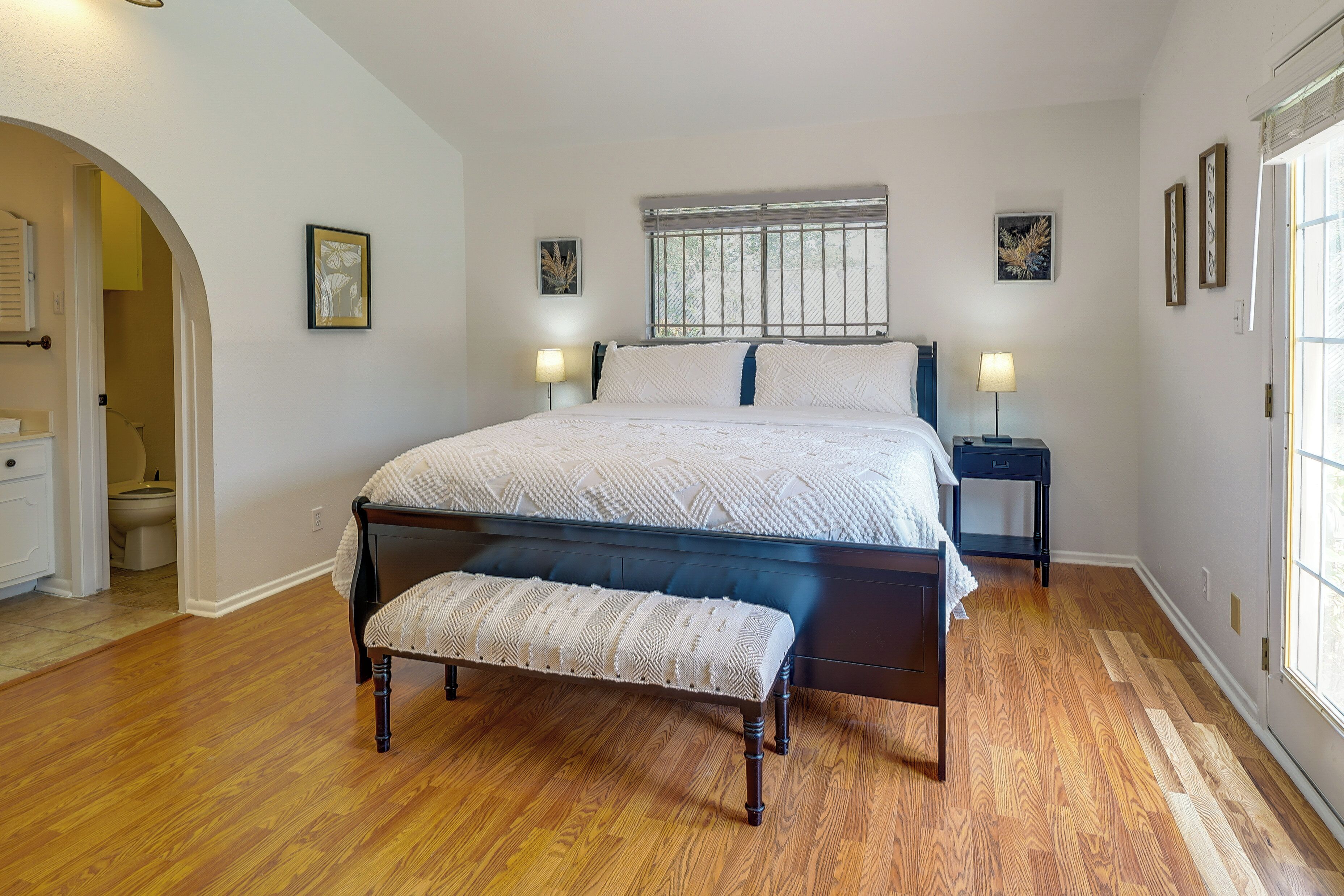 A bedroom with a large bed, bedside tables, a bench, and a window with blinds.
