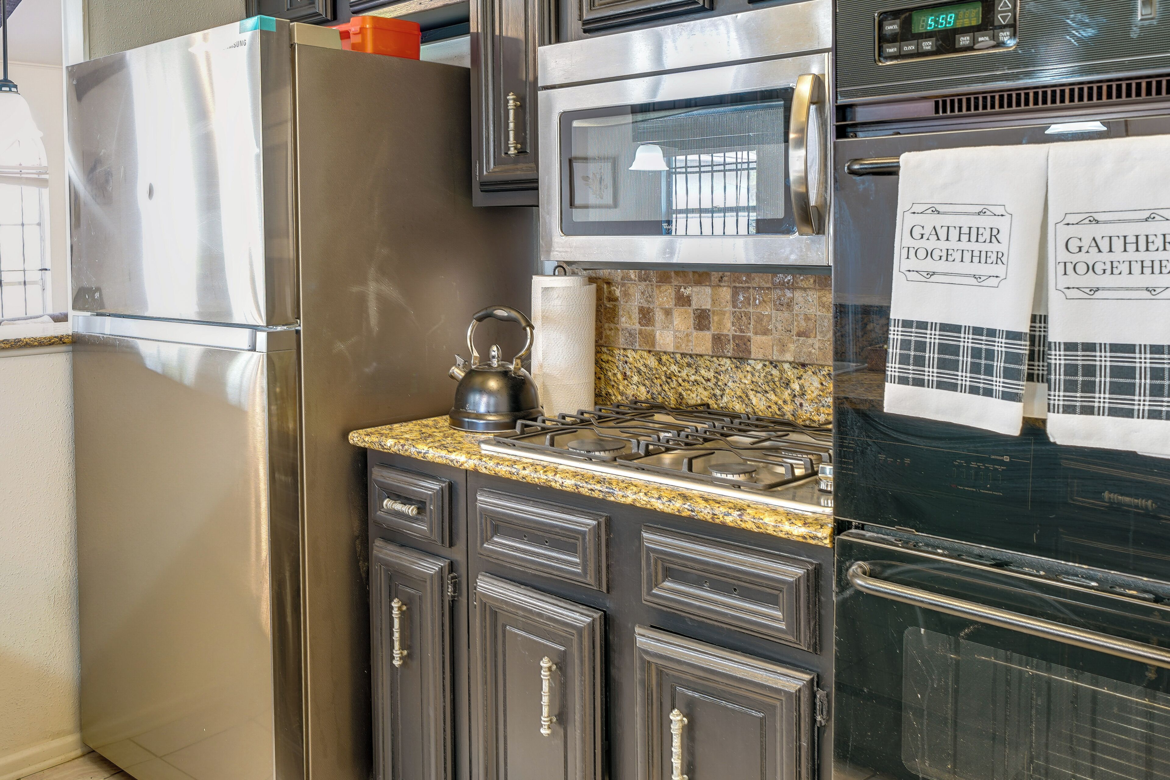 A kitchen with stainless steel appliances, dark cabinetry, and a granite countertop.