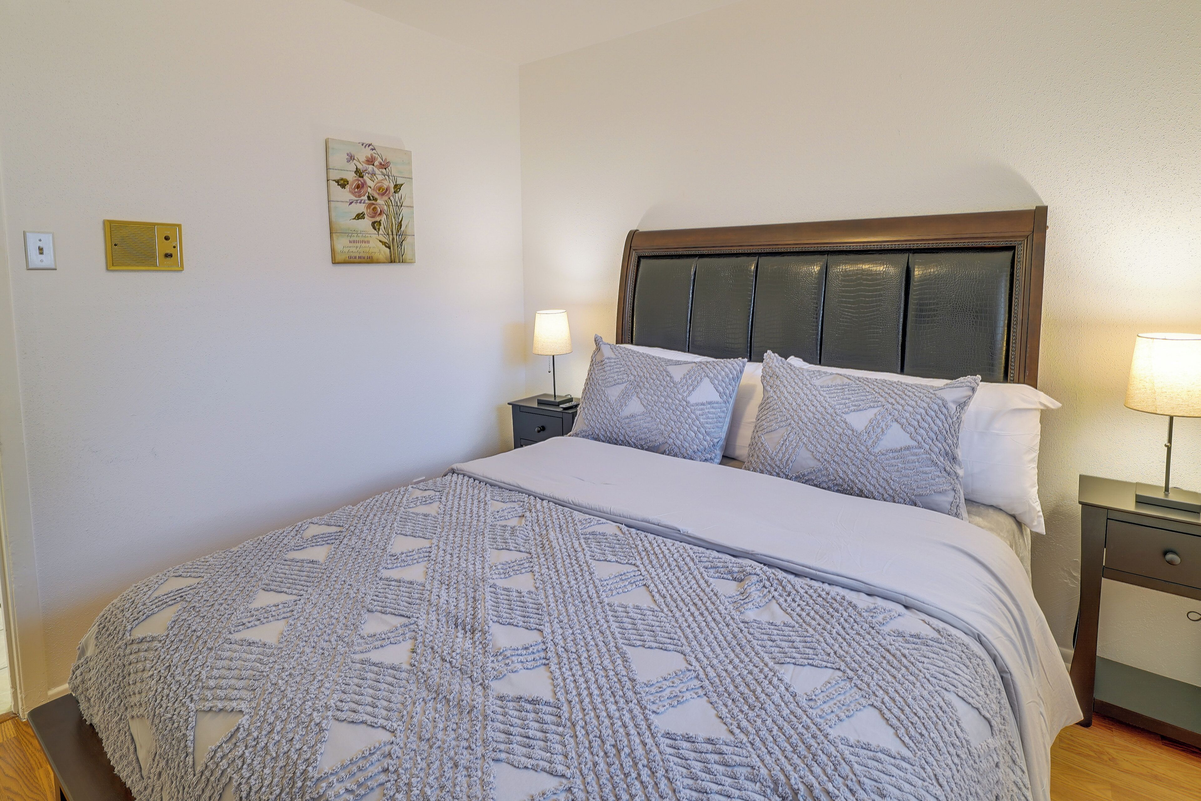 Un lit bien fait, avec une couvre-lit à motifs, une tête de lit en bois et deux lampes de chevet.