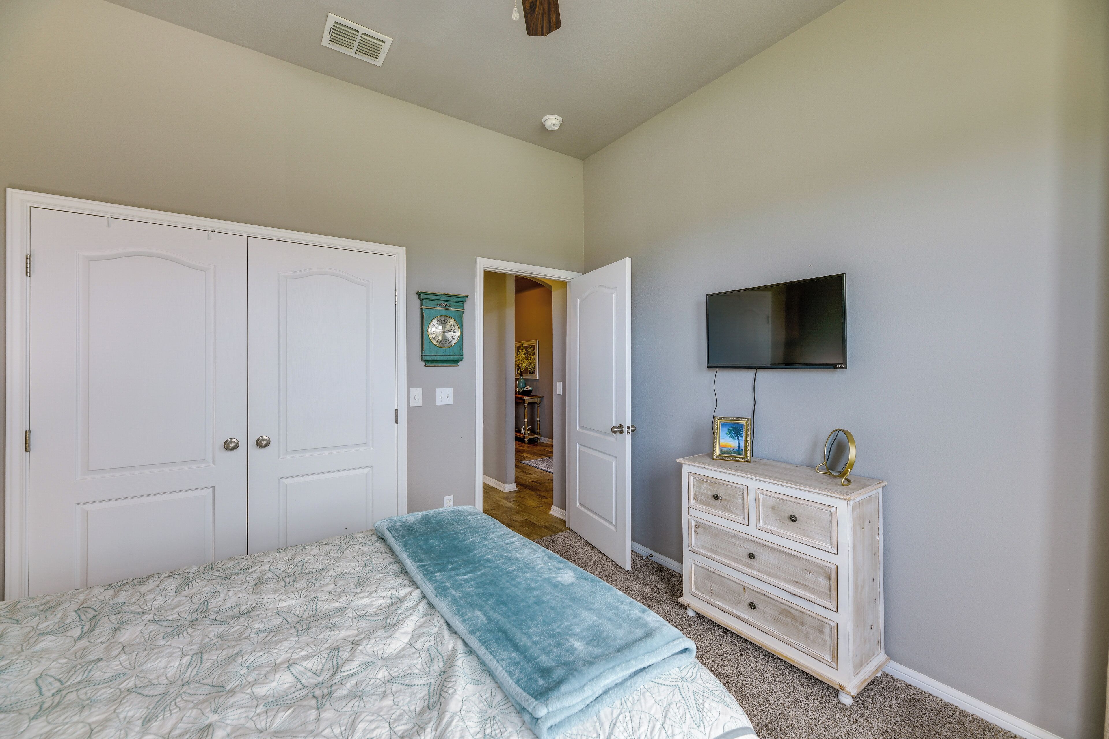 Un dormitorio con una cama, un tocador, un televisor y una puerta que da a otra habitación.