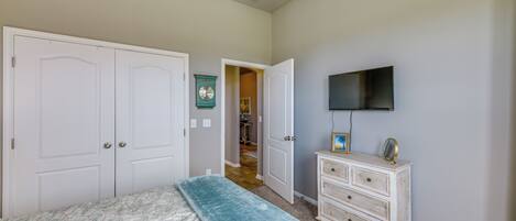 Un dormitorio con una cama, un tocador, un televisor y una puerta que da a otra habitación.
