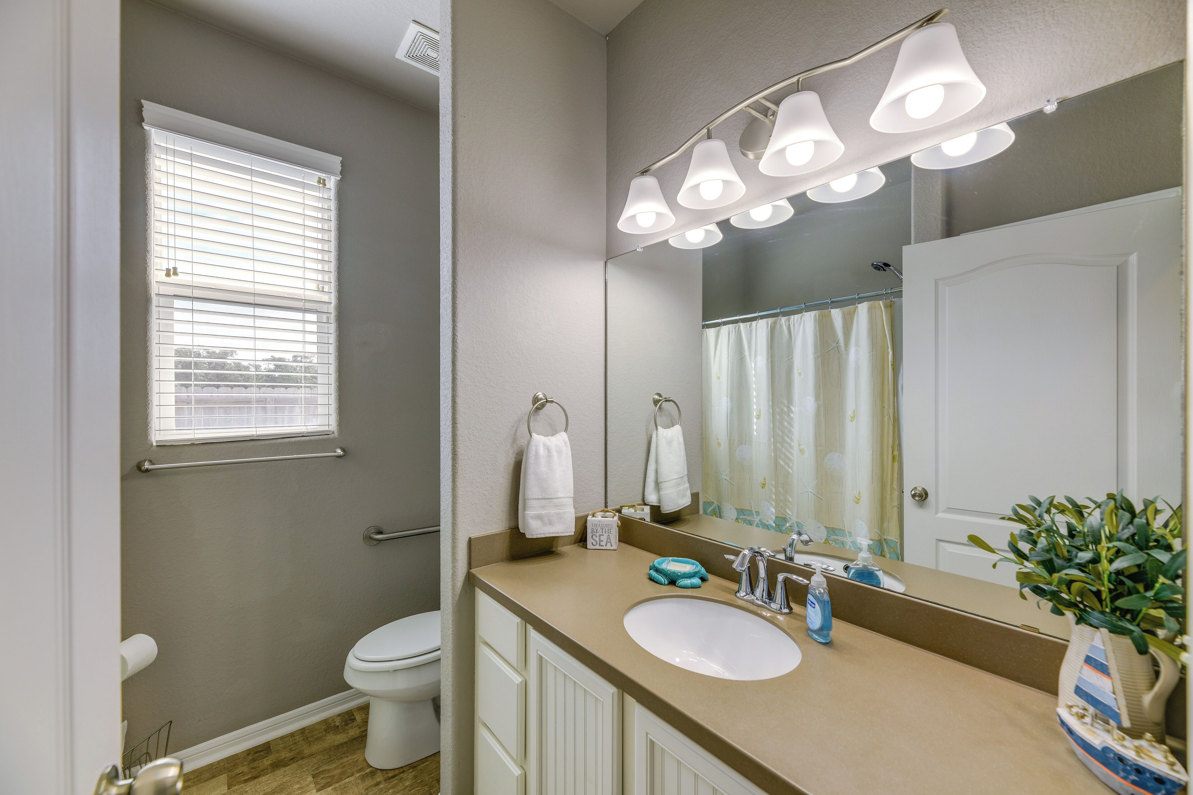 A bathroom with a white toilet, a beige vanity with a sink, a mirror, and a window with blinds.