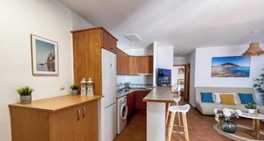 A compact kitchen with wooden cabinets, a central island, and a dining area with a sofa and bar stools. - El Velero Curry (San José)