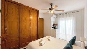 Quarto com um guarda-roupa grande, um ventilador de teto, uma cama com almofadas e uma janela com cortinas.