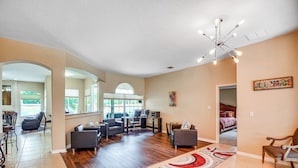 A spacious living area with a large rug, wooden flooring, and a modern chandelier. - Palm Coast Retreat w/ Heated Pool & Private Patio! (Palm Coast)