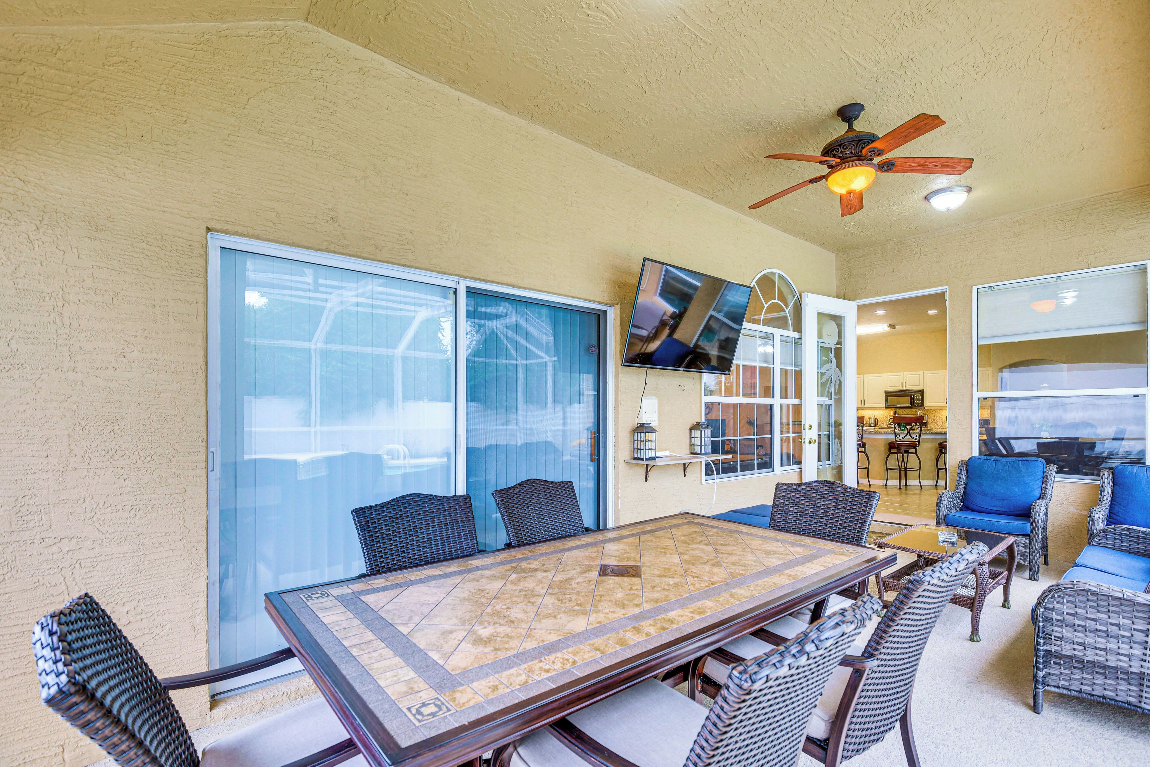 A sunlit patio with a glass door, a dining table with chairs, and a ceiling fan.